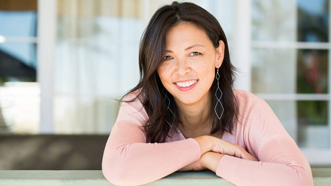 Smiling person with arms crossed leaning on a railing