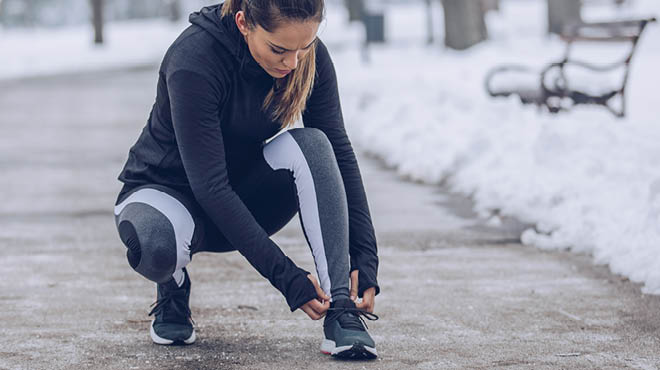 Crouching on sidewalk in winter, tying shoelaces