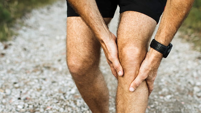 Hands holding knee joint while on gravel walking path