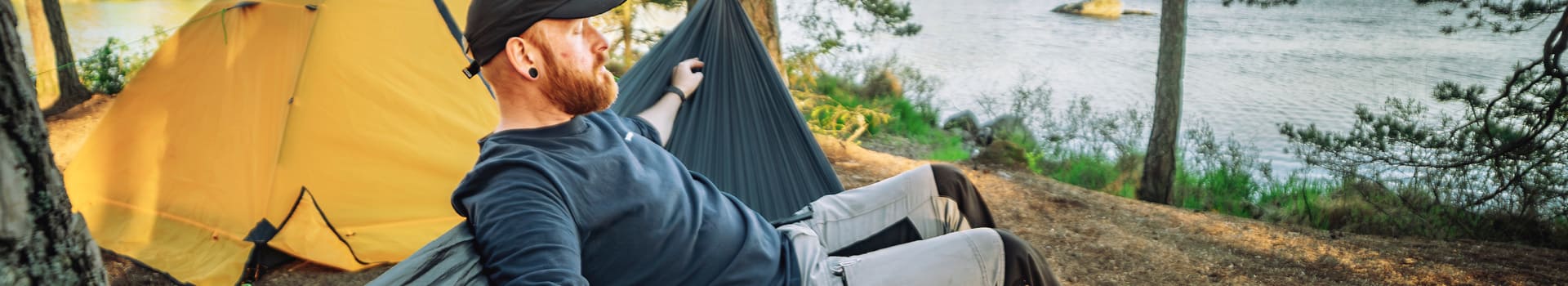 Person sitting on hammock in wooded area.